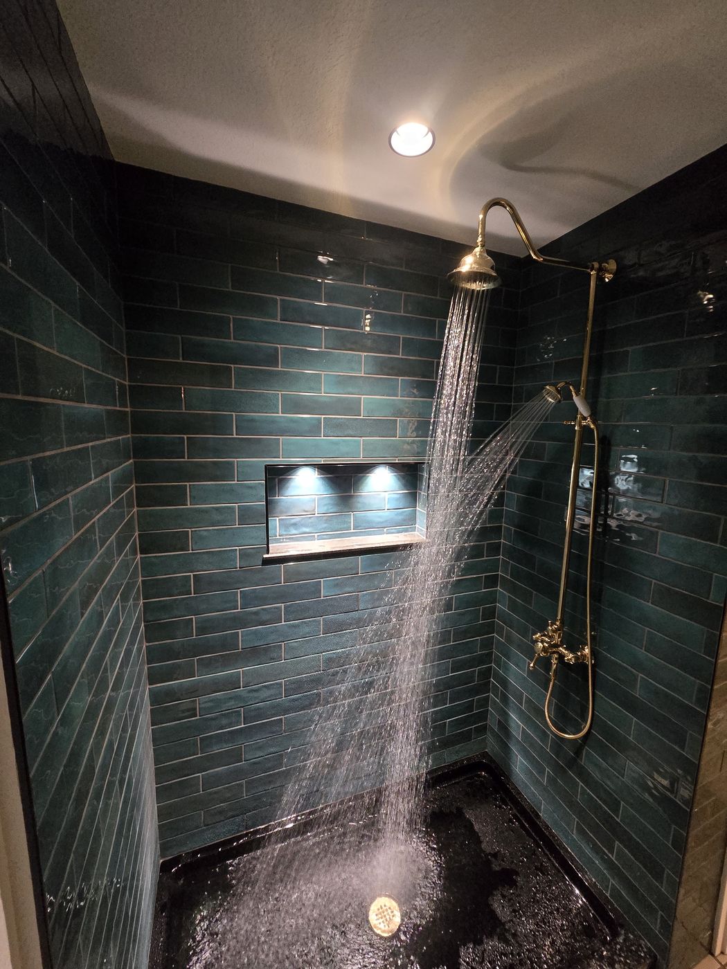 Finished tiled shower with unlacquered brass rain head and handheld, water running