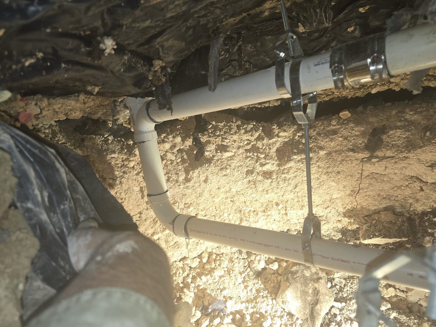 A drain line in a tunnel under a slab, hung from the slab on threaded rod