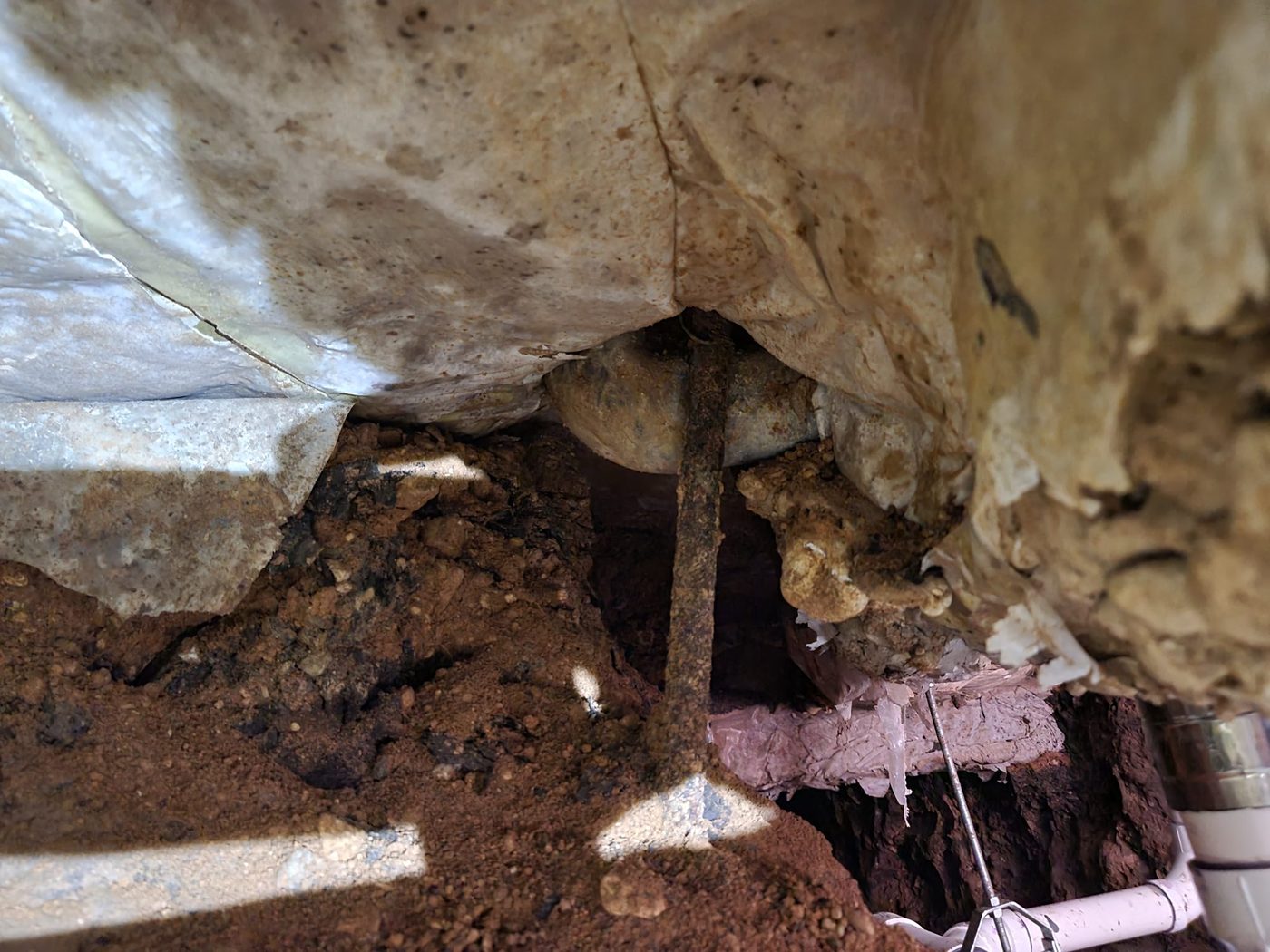 A corroded original drain line under a slab with the new PVC line run in beside it