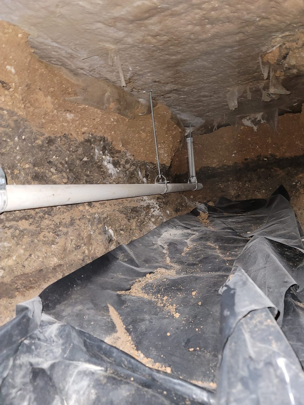 A new drain line running the length of a tunnel, hung from the slab on two threaded rods