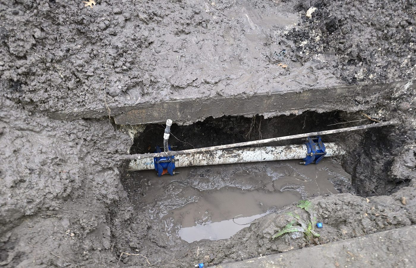 A water main repair under a concrete walk, held with two repair clamps